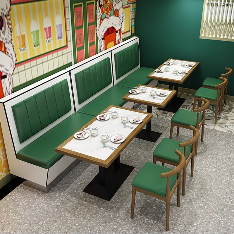 A rock slab dining table with a sleek rectangular top, supported by black legs, paired with green upholstered chairs in a stylish restaurant interior.