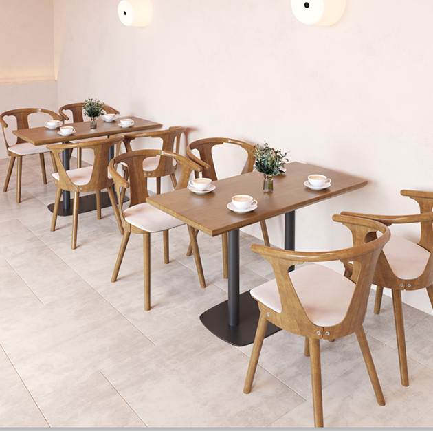 A cozy café setting with round wooden tables featuring dark metal bases and comfortable wooden chairs with soft white cushions.