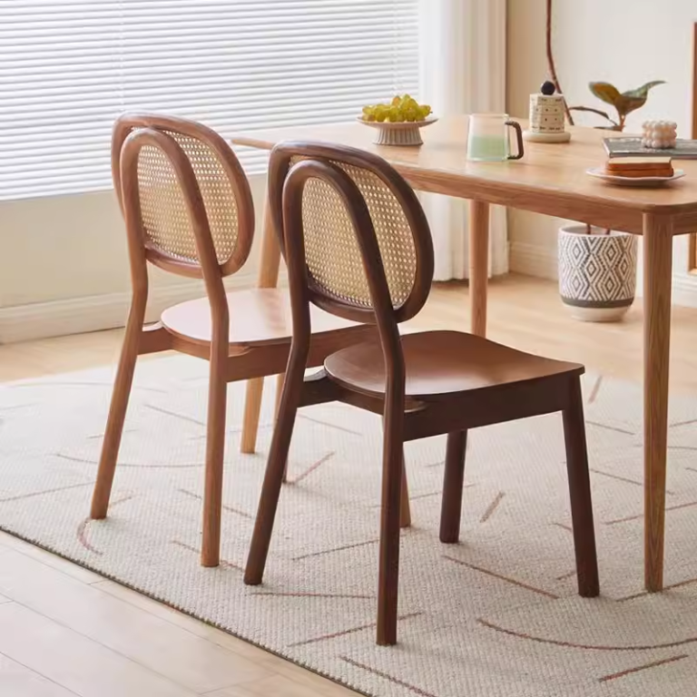 Two wooden cane back chairs with contrasting finishes at a dining table in a bright and cozy room with a soft rug.