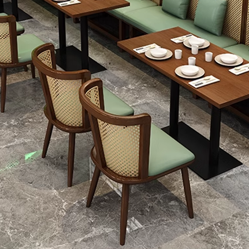 Wooden cane chairs with cushioned seats arranged around tables in a restaurant setting with gray flooring and green accents, minimalist design