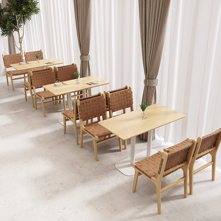 Woven leather chairs with beige wooden frames placed around light wood tables in a modern dining room.